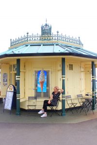 Katharina sitzt auf einem Stuhl vor einem Pavillon in Brighton